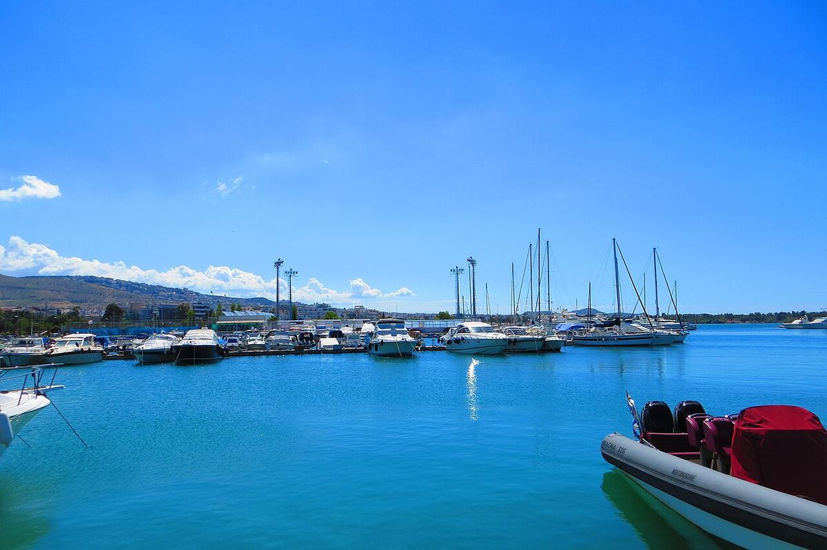 Γαλάζια νερά και ιστιοφόρα στη μαρίνα της Γλυφάδας με βουνά στο βάθος